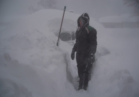 woman standing next to car buried in snow. 
