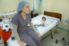 Nurse sitting on bed with sleeping child patient. 