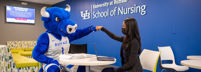 Student fist bumping mascot in nursing lounge. 