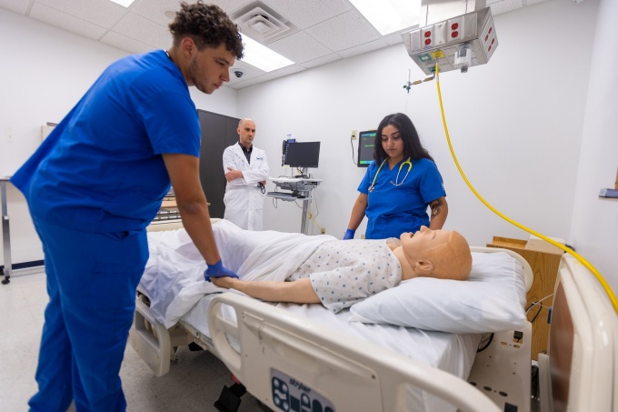 Nursing students holding the hand of a computerized manikin experiencing simulated death. 