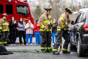 Firefighters using the Jaws of Life to open a vehicle while nursing students observe in the background. 