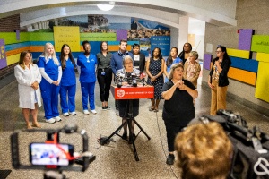 Annette Wysocki standing at media podium flanked by nursing students and faculty. 