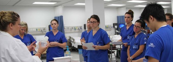 nursing students listening to clinical instructor in skills lab. 