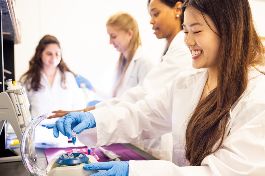 Several researchers in white lab coats at lab bench. 
